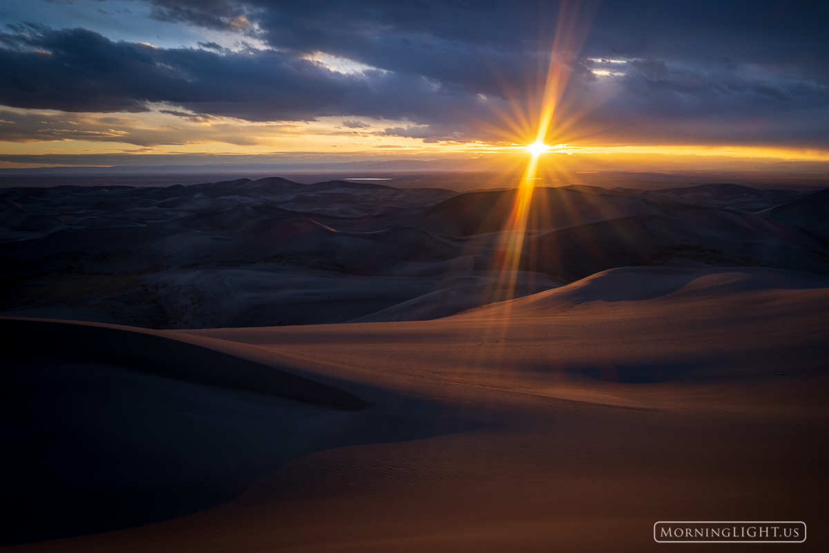 As the day comes to an end in Great Sand Dunes National Park, the sun briefly appears before setting, creating a dramatic sunstar...